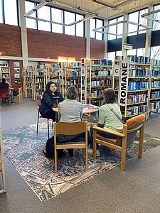 Drei Personen sitzen an einem Tisch in der Bibliothek.