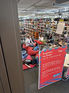 Blick durch eine Glastür auf ein auf Kissen sitzendes Publikum