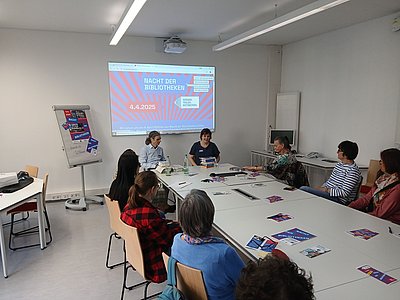 Mehrere Personen sitzen an einem Konferenztisch und blicken auf eine Präsentation