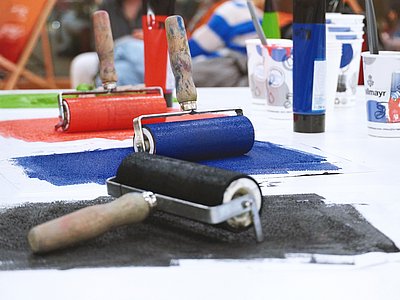 Drei Farbwalzen mit verschiedenen Farben auf einem Tisch