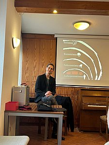 Eric Seuberth sitzt auf einem Tisch vor einer Präsentationsleinwand