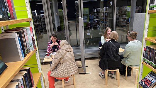 Mehrere Personen sitzen an zwei kleinen Tischen zusammen.