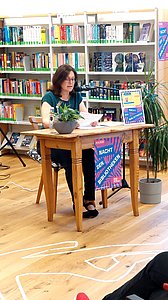 Ines Küffner sitzt an einem Tisch und liest vor.